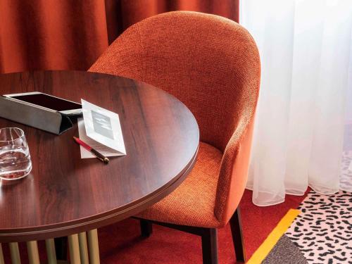 a wooden table with a chair next to a table with a glass at Nest Hotel Paris la Défense - MGallery Collection in Puteaux
