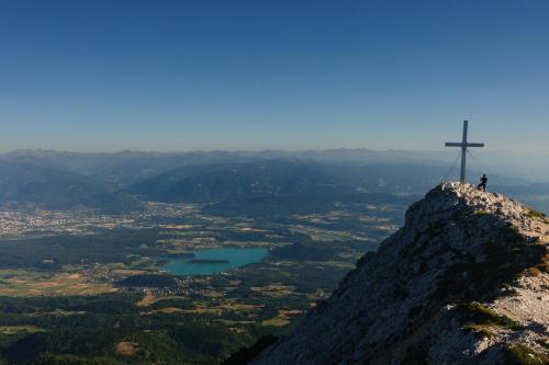 a man standing on top of a mountain with a cross at Gästehaus Trink B&B in Drobollach am Faakersee