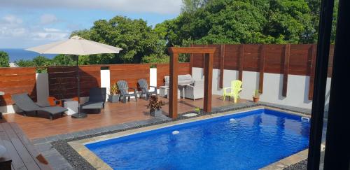 a swimming pool with chairs and a table and an umbrella at La Villa JoLi in Saint-Joseph