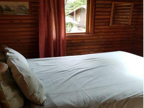 Cama blanca en habitación con ventana en Eland Valley Resort en Underberg