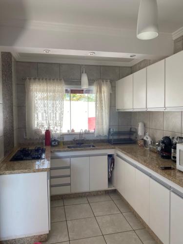 een keuken met witte kasten, een wastafel en een raam bij CASA FAMILIAR “SANTA PAZ” in Aparecida