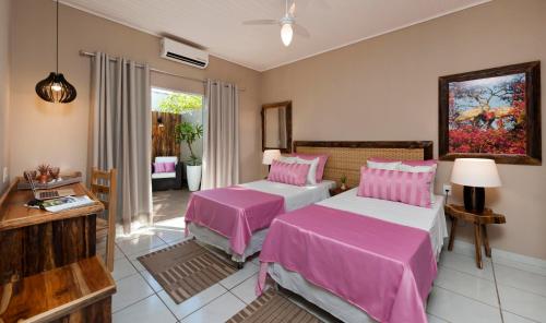 two beds in a room with pink sheets at Pousada Rio Claro in Poconé