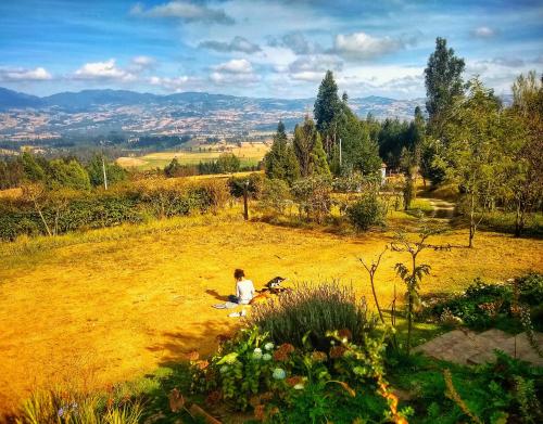 a person is sitting on a grassy hill at Cabaña Agrreste in Nemocón