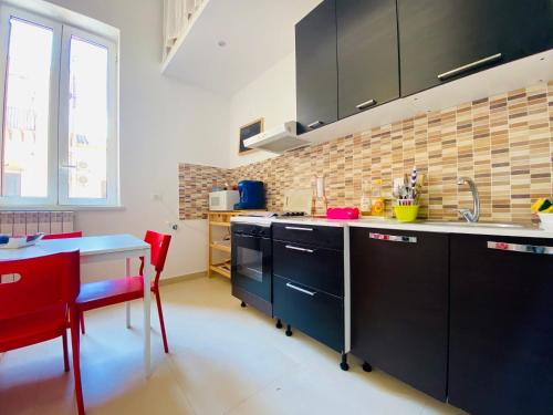 a kitchen with black cabinets and a table and red chairs at Liolà Home Palermo in Palermo
