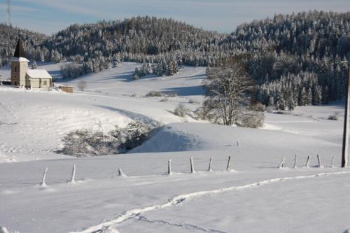 a snow covered field with a church in the distance at Gîte comme à la maison -12 pers- La Cabiote in Les Piards