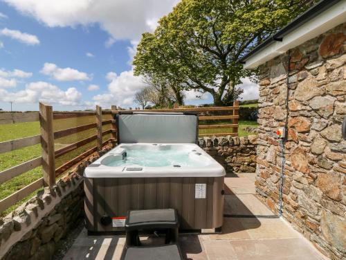 a hot tub on a patio next to a stone wall at Beudy Tyddyn in Llandyfrydog