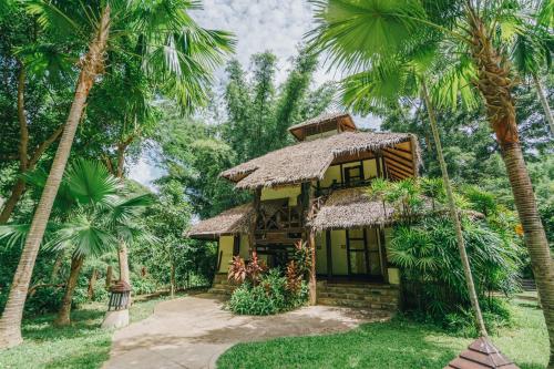 a small house in the middle of palm trees at River Kwai Resotel in Sai Yok
