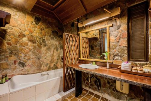 a stone bathroom with a tub and a sink and a tubermott at River Kwai Resotel in Sai Yok