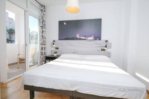 a white bedroom with a large bed and a window at Apartamentos Ibiza in Colonia Sant Jordi