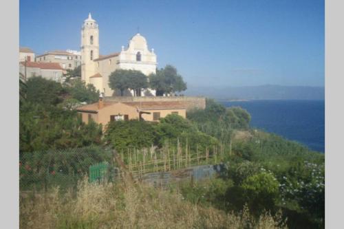 un bâtiment au sommet d'une colline à côté de l'océan dans l'établissement Grande maison au cadre verdoyant au centre village, à Cargèse