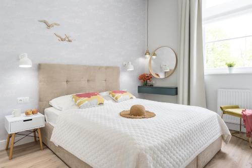 a white bedroom with a bed with a hat on it at Sanhaus Apartments - Apartament Mera z parkingiem i klimatyzacją in Sopot