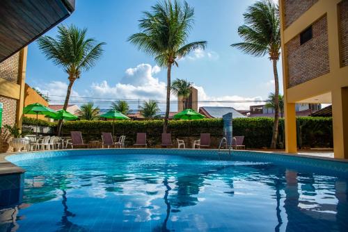 a swimming pool with chairs and palm trees at Pizzato Praia Hotel in Natal