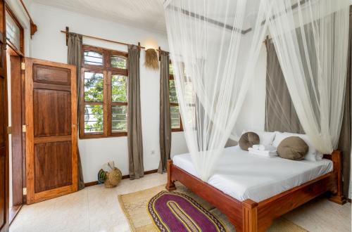 um quarto com uma cama com cortinas e uma porta em KIMA Serviced Beach House & Suites em Bwejuu