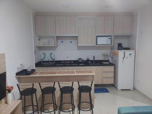 a kitchen with a counter and three bar stools at Residencial Flats Botanicus 1 in Olímpia