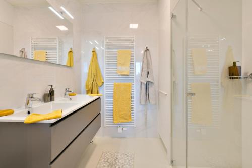 een badkamer met een wastafel en een douche met gele handdoeken bij Modern appartement met doorkijk op de duinen in Cadzand