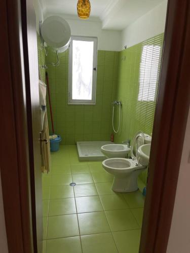 zielona łazienka z 2 toaletami i oknem w obiekcie Eldi's Apartment w mieście Shëngjin