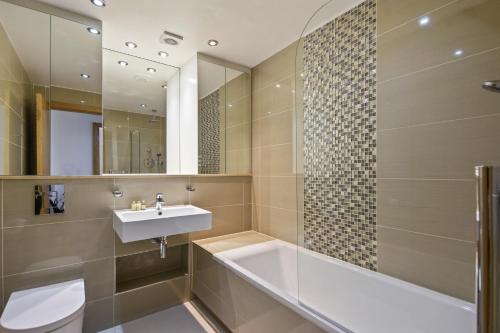 a bathroom with a sink and a tub and a mirror at Cambric by Aeria Apartments in London