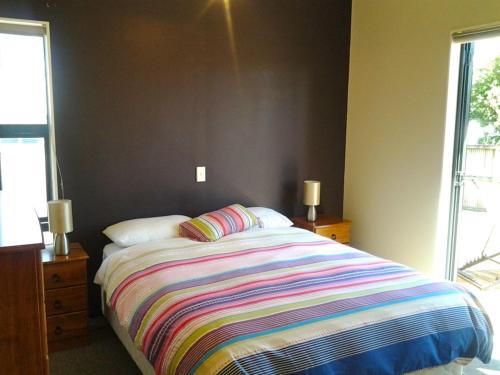 1 dormitorio con 1 cama con una manta a rayas de colores en Puka Bach - Matarangi Holiday Home, en Matarangi