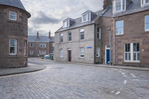 an empty cobblestone street in front of brick buildings at Stonehaven ground floor home with a spectacular harbour view. in Stonehaven