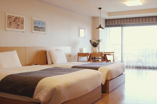 zwei Betten in einem Hotelzimmer mit Tisch und Stühlen in der Unterkunft Luceville in Seogwipo