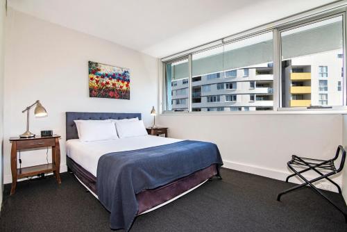 a bedroom with a bed, desk, chair and lamp at Ridge Apartment Hotel in Brisbane