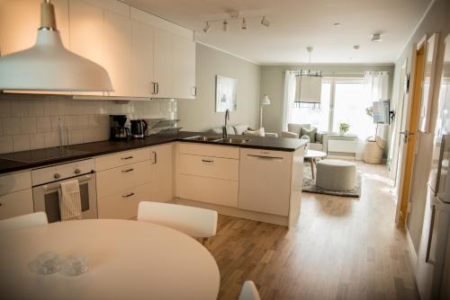 a kitchen with white cabinets and a table and a living room at Sky Hotel Apartments Valla Berså in Linköping