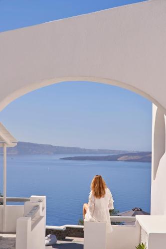 a woman sitting on a bench looking at the water at Mr and Mrs White Oia - Santorini in Oia