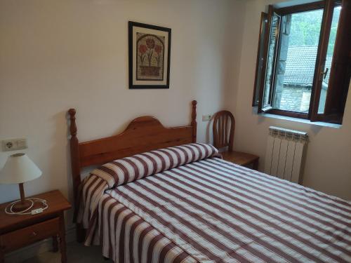 a bedroom with a bed with a striped comforter and a window at Centro Torla 4pax Apartamento in Torla-Ordesa