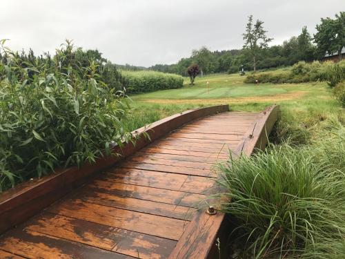a wooden boardwalk in a field of grass with a horse in the background at Golf&Wellness Resort Alfrédov in Alfrédov