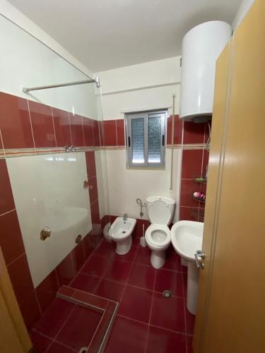 baño de azulejos rojos con aseo y lavamanos en Jasmine Apartments, en Sarandë