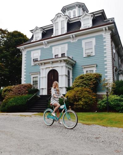 a girl riding a bike in front of a blue house at The Hotel Marblehead in Marblehead