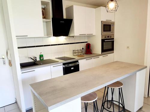 une cuisine avec des armoires blanches et un comptoir avec des tabourets dans l'établissement Charmant appartement avec terrasse et jardin au calme Proche Bus Métro, à Toulouse