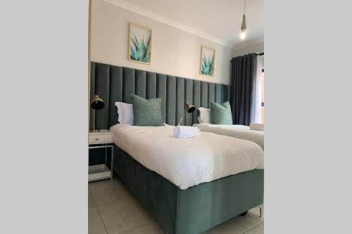 a bedroom with two beds and a green headboard at Stay Upmarket at The Blyde in Boschkop