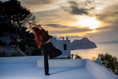 a woman dancing on a wall with the ocean in the background at Uranos Studios in Amorgos