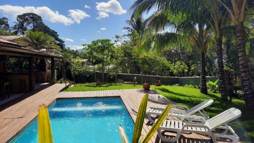 un patio trasero con piscina, sillas y árboles en Moana Ilhabela en Ilhabela