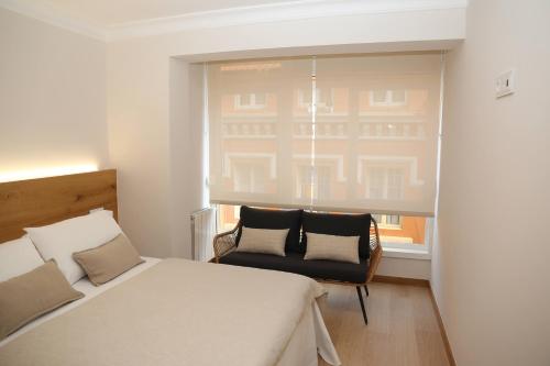 a bedroom with a bed and a chair and a window at Apartamento Orzán playa in A Coruña