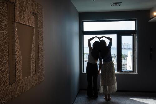 Una pareja de pie en una habitación mirando por la ventana en Hotel Cocktail Stay Naha en Naha