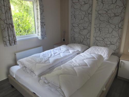 a bed with white sheets and a window at Chalet Wanama. Gelegen op het vakantiepark Het Lierderholt op de veluwe. in Beekbergen