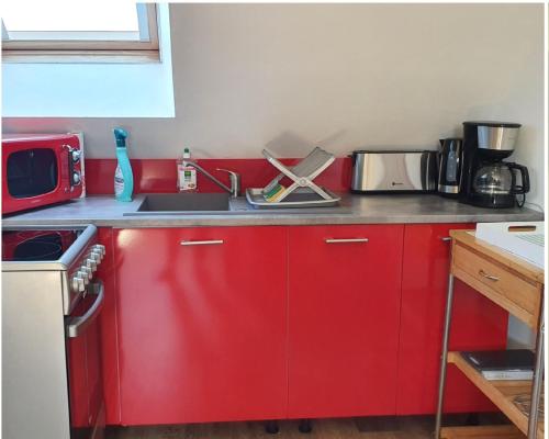 cocina roja con fregadero y microondas en Côte de Nacre, en Douvres-la-Délivrande