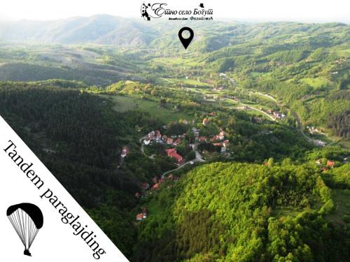 a paraglider flying over a lush green valley with a town at Ethno Village Bogut in Bogutovac