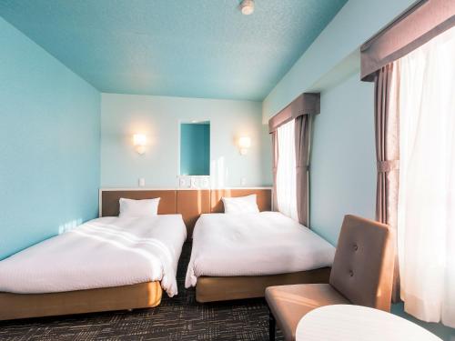 a room with two beds and a chair in it at Hotel Wing International Chitose in Chitose