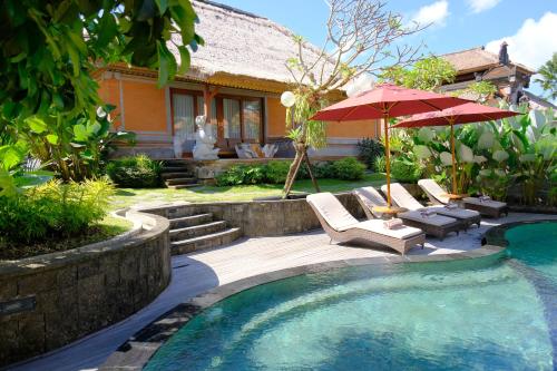 a pool with chairs and an umbrella next to a house at Puri Andong Villa in Ubud