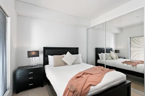 a white bedroom with two beds and a mirror at Astra Apartments Perth CBD in Perth