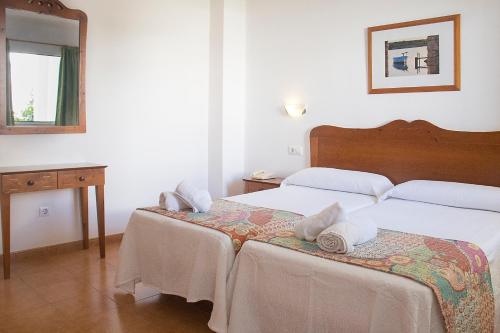 a bedroom with two beds and a table and a mirror at Hotel Geminis in Ciutadella