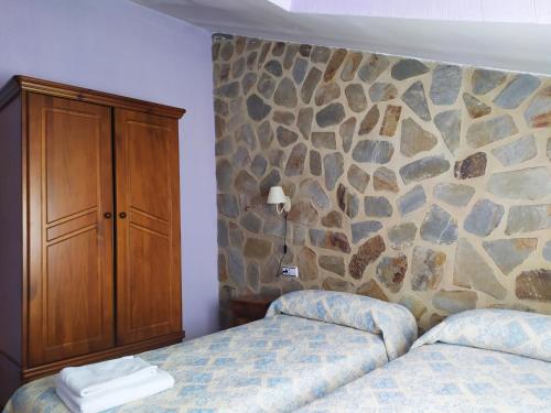1 dormitorio con 2 camas y pared de piedra en Tejadillos - Apartamentos El Cabo en Las Majadas