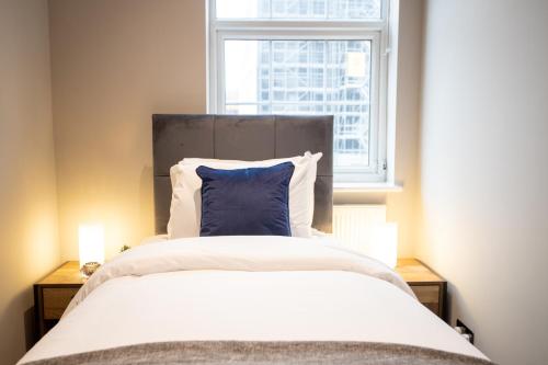 a bed with a blue pillow in front of a window at Deluxe Modern 1&2 Bed Apartments Near Brighton Beach & Station in Brighton & Hove
