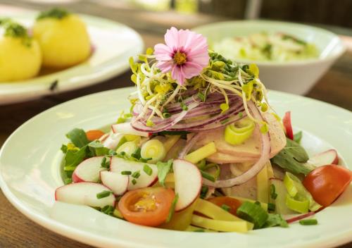 a white plate with a salad with a flower on it at Naturschlosshotel Blumenthal in Aichach