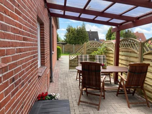 un patio con una mesa de madera, sillas y una pared de ladrillo en Ferienhaus Ronny, en Hinte