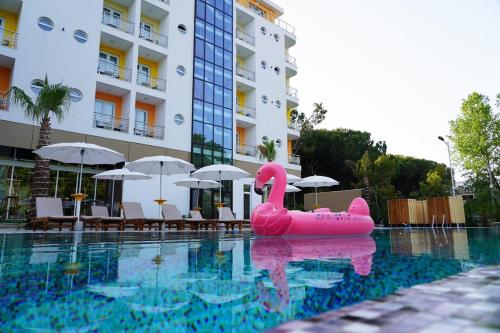 un cigno rosa gonfiabile in una piscina accanto a un edificio di Hotel Monaco & Garden a Golem