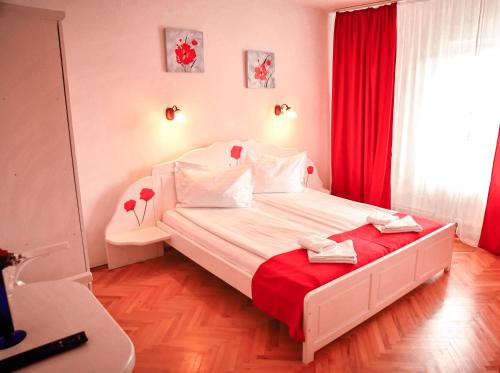 a bedroom with a white bed with a red curtain at Pensiunea Vila Silva I in Haţeg